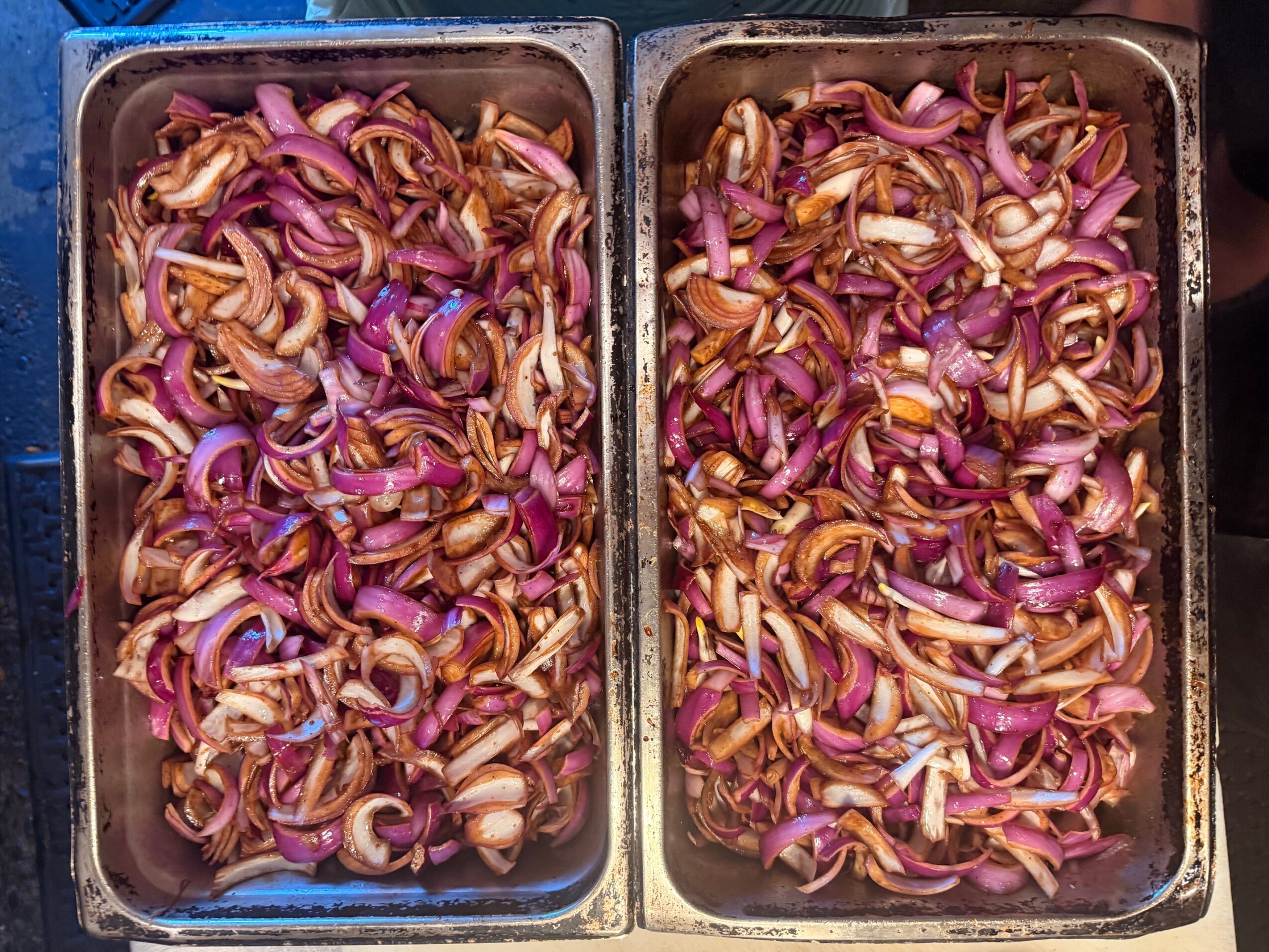 Two metal trays filled with sliced red onions and other vegetables.