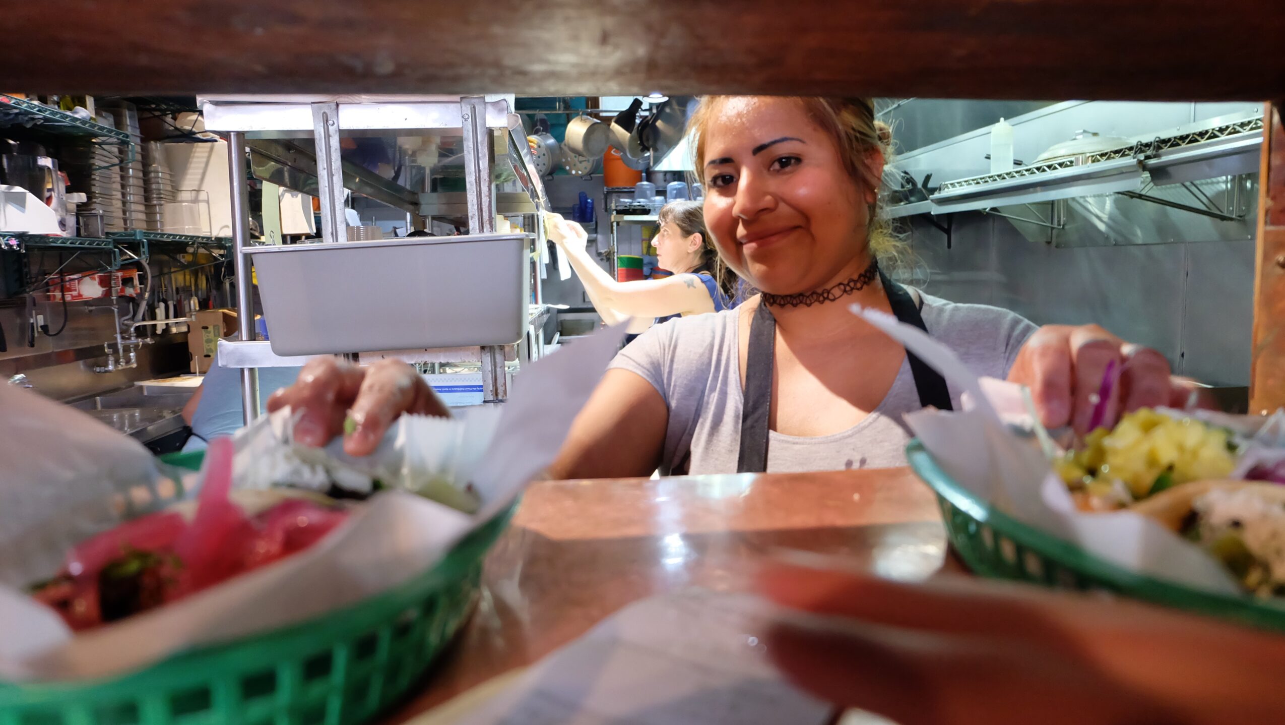 A person prepares food behind a counter with baskets of ingredients in the foreground.