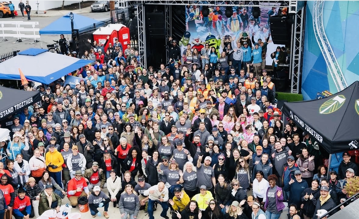 Large crowd gathered in front of an event stage, with tents and a track visible nearby.