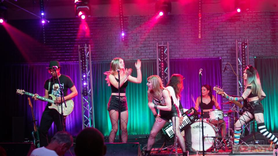 A band performs onstage under colorful lights, with a singer at the microphone and musicians playing guitars and drums.