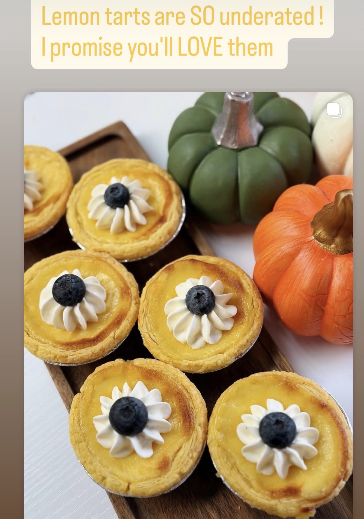 Lemon tarts topped with cream and blueberries sit beside green and orange decorative pumpkins.