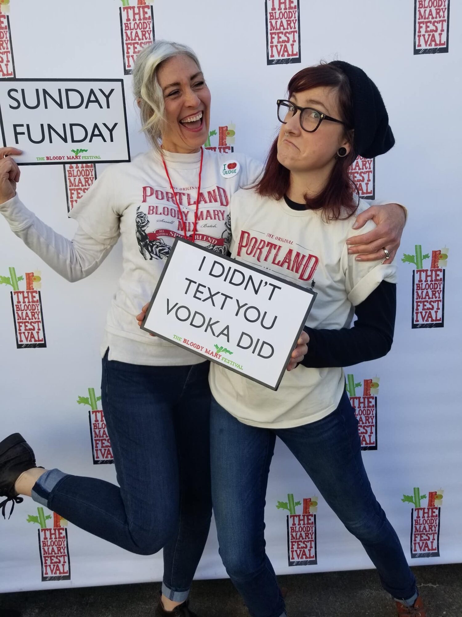 Two people pose with signs reading “Sunday Funday” and “I didn’t text you, vodka did.”