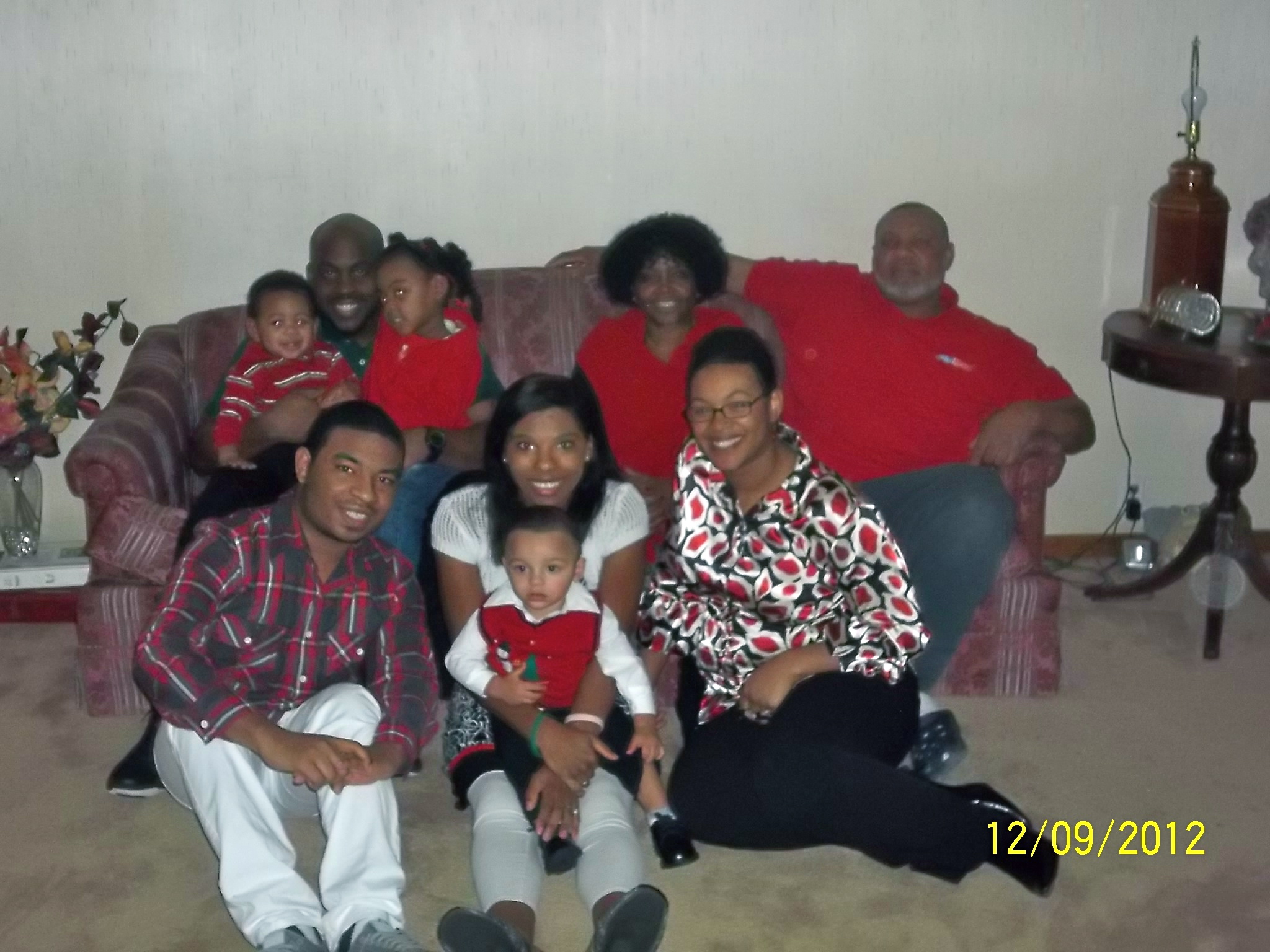 A group of adults and children pose together in front of a patterned couch.