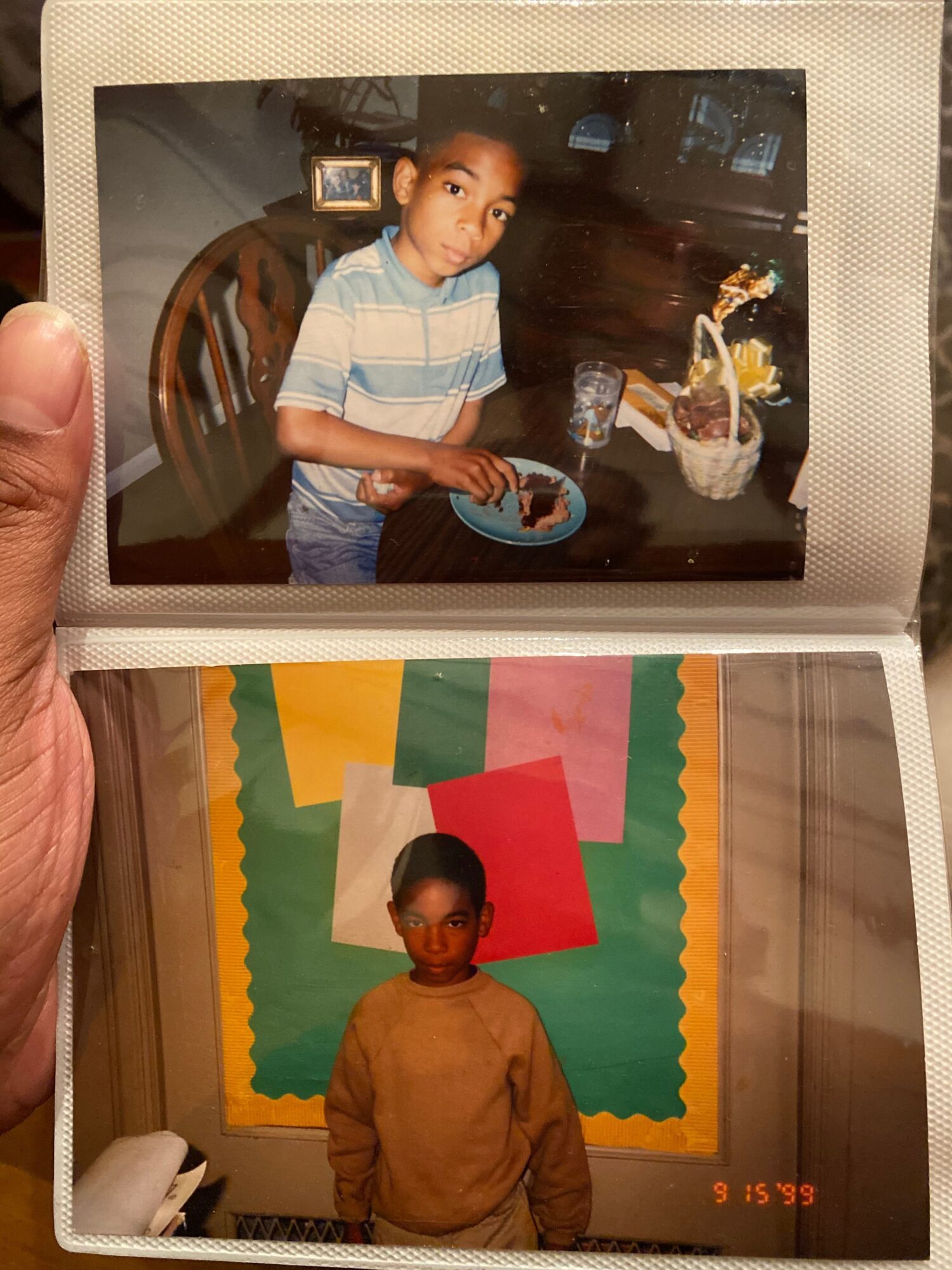 Open photo album showing two printed photos, including a child near a chair and a person standing before a colorful backdrop.