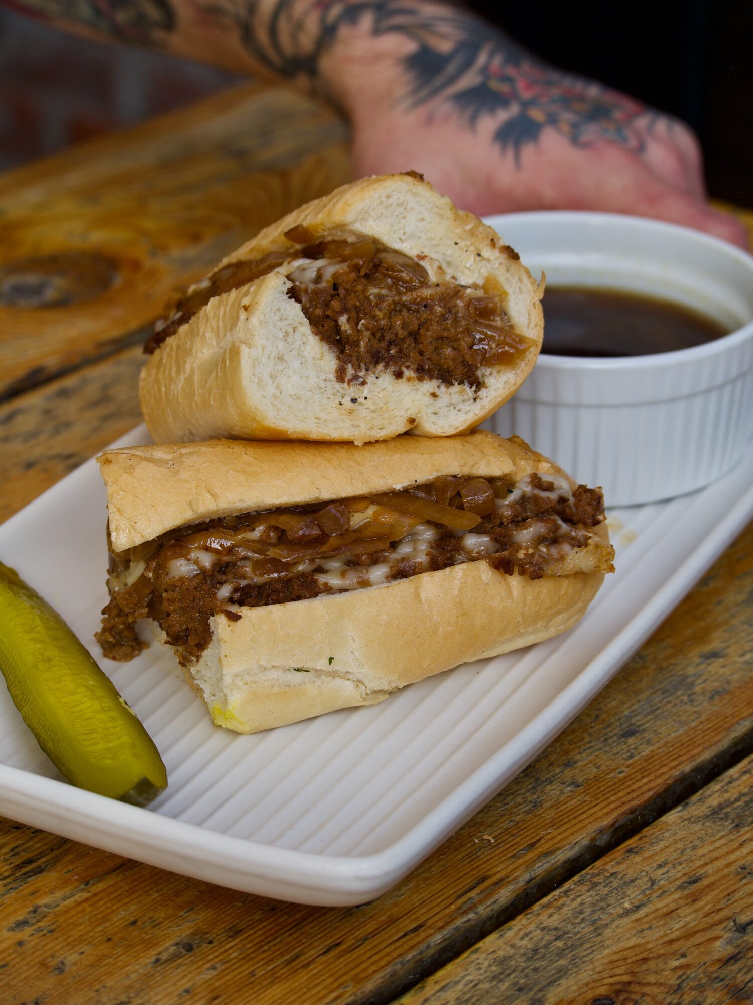 Two meat-filled sandwich halves on a white tray beside a cup of dark liquid and a green pepper.