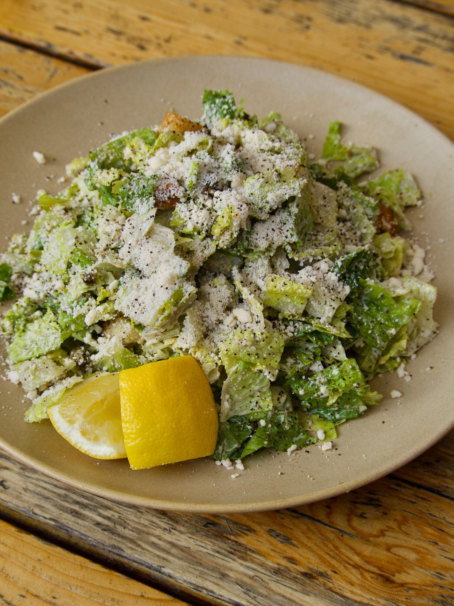 A plate of chopped green salad topped with grated cheese, alongside a lemon wedge and peel.