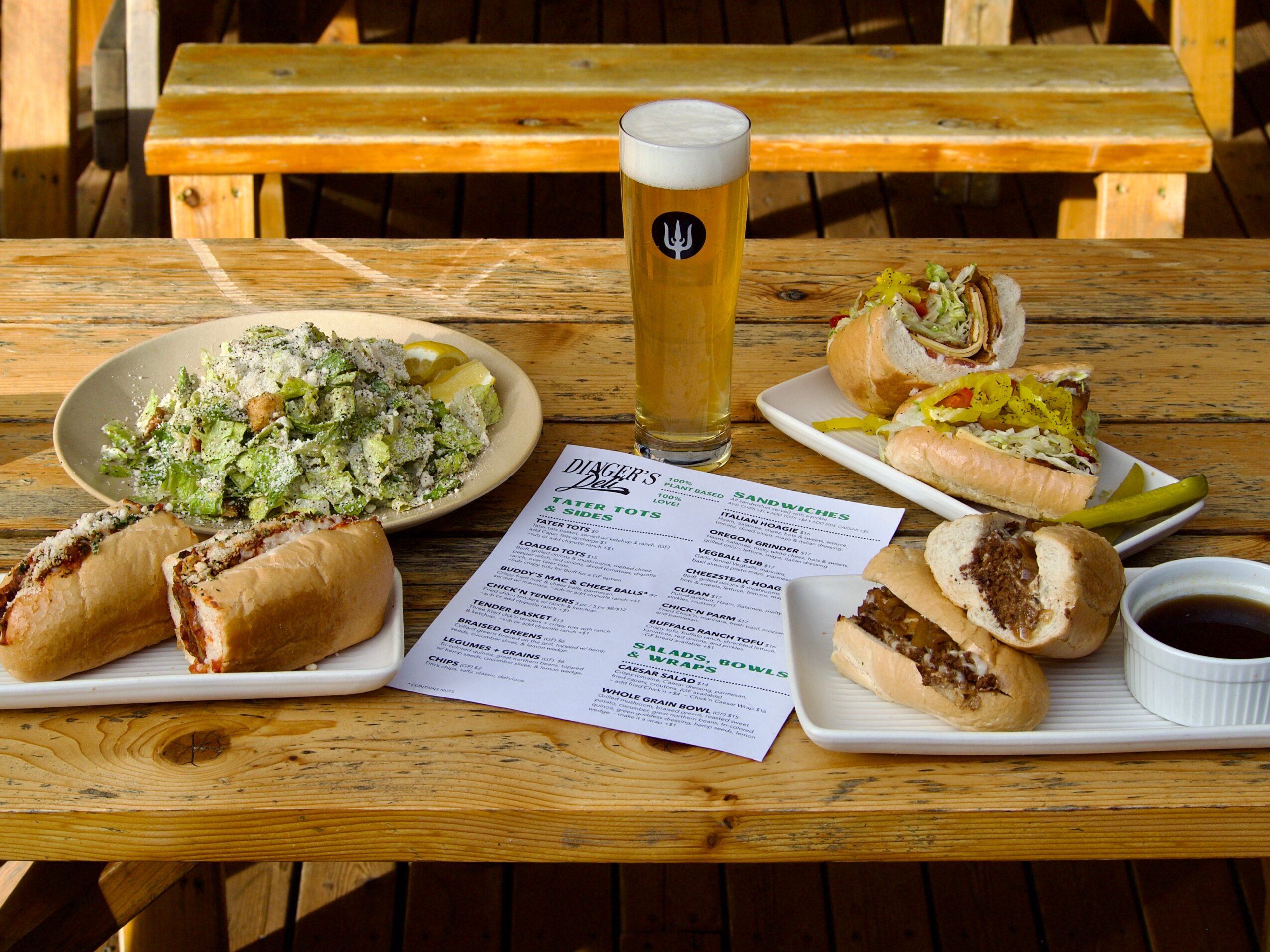 A wooden table holds a salad, sandwiches, a drink, and a printed menu.