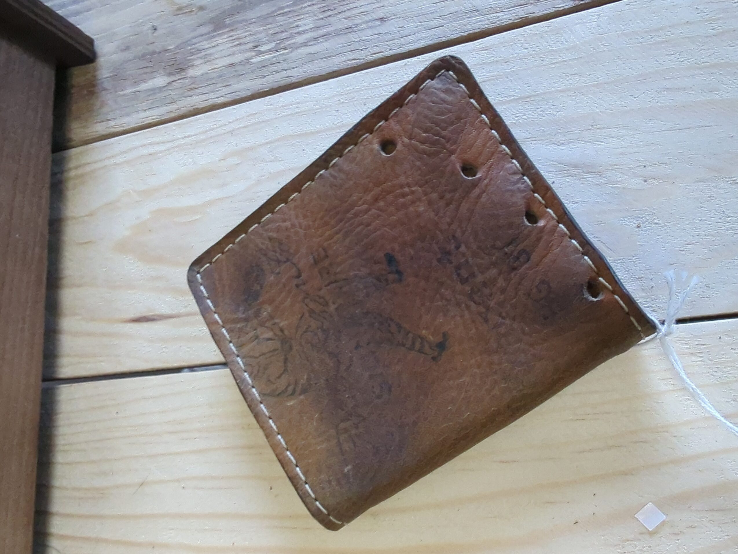 Worn brown leather pouch resting on a pale wooden plank surface.