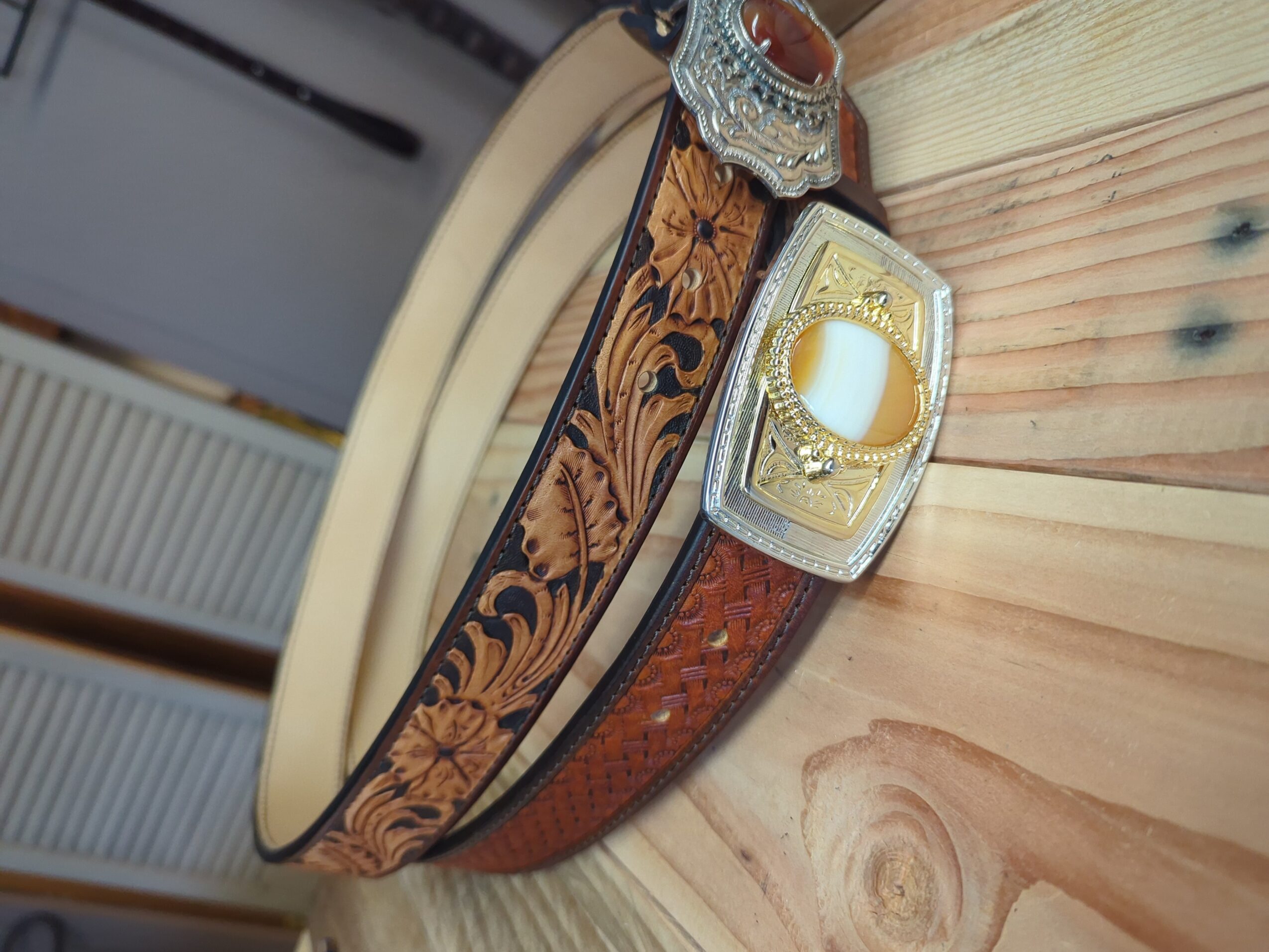 Decorative leather belt with ornate metal buckles hanging against a wooden wall.