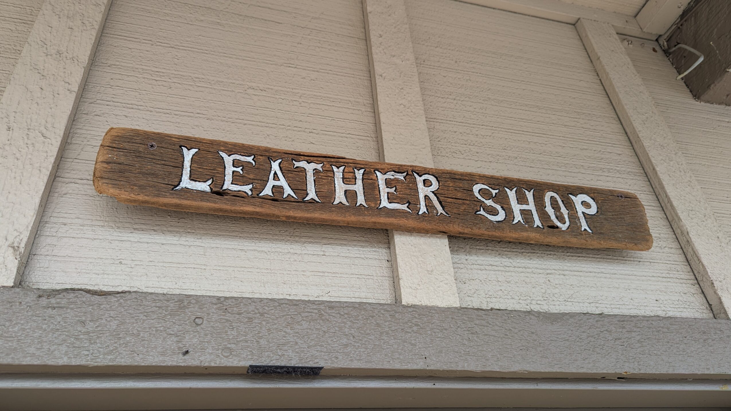 A wooden sign reading “LEATHER SHOP” mounted above a doorway.