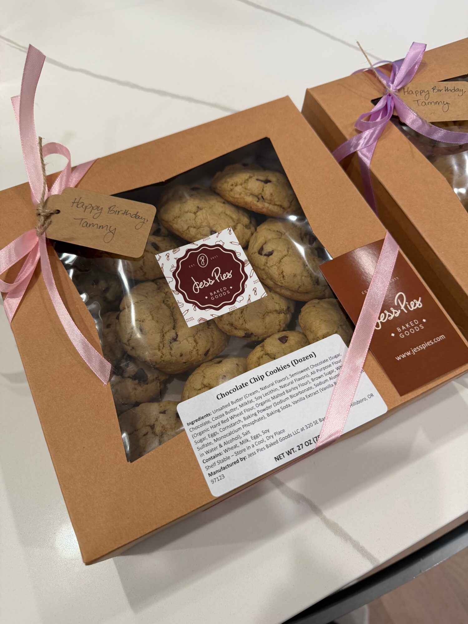 Two brown gift boxes tied with pink ribbons, one displaying a clear window filled with cookies.