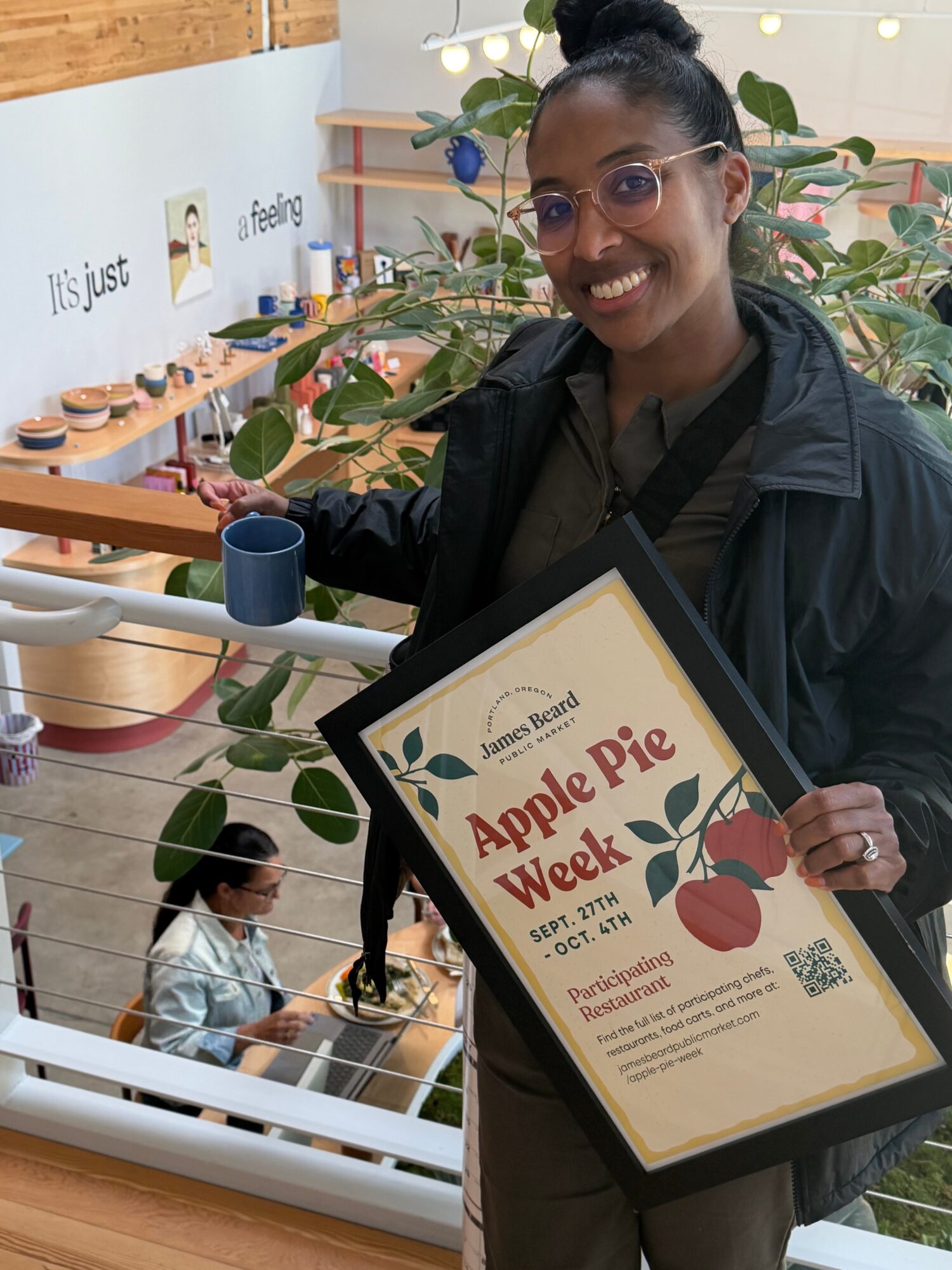 Person holding an Apple Pie Week certificate beside a display of pies and plants.