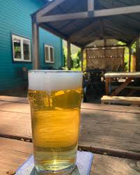 A glass of golden beer sits on a wooden picnic table beneath a covered outdoor patio.
