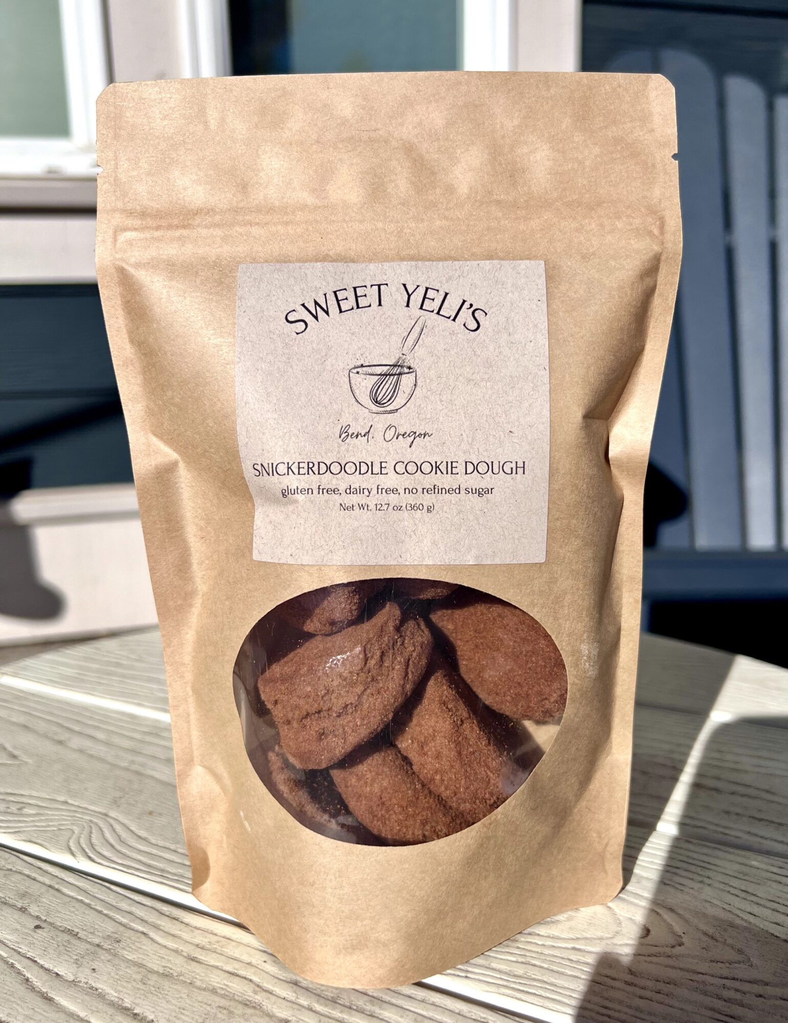 A kraft paper pouch labeled “Sweet Yelis” with a clear window showing chocolate cookie dough, standing on a sunlit table.