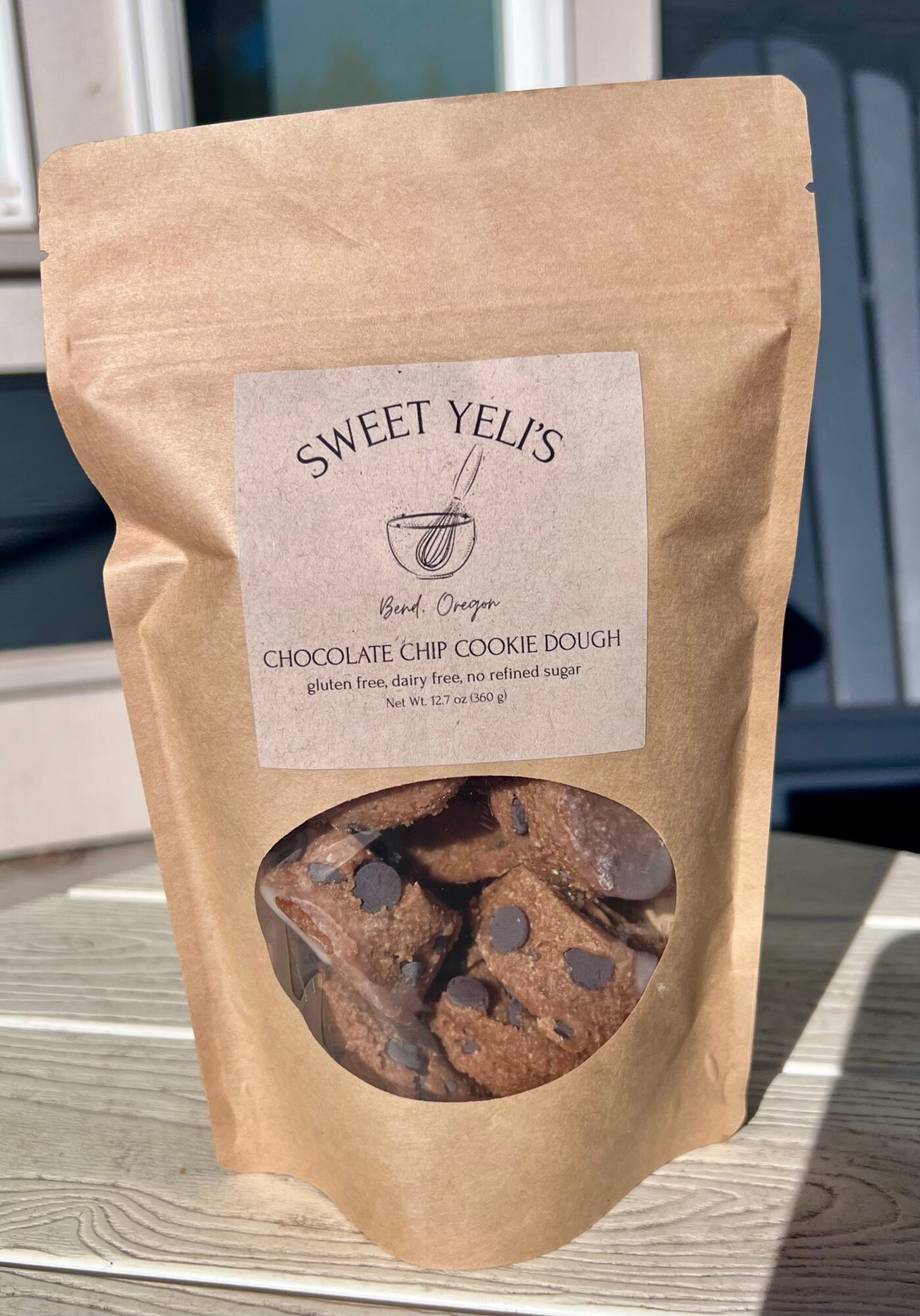 A kraft paper pouch labeled Sweet Yels sits on a wooden table, with a window behind it.