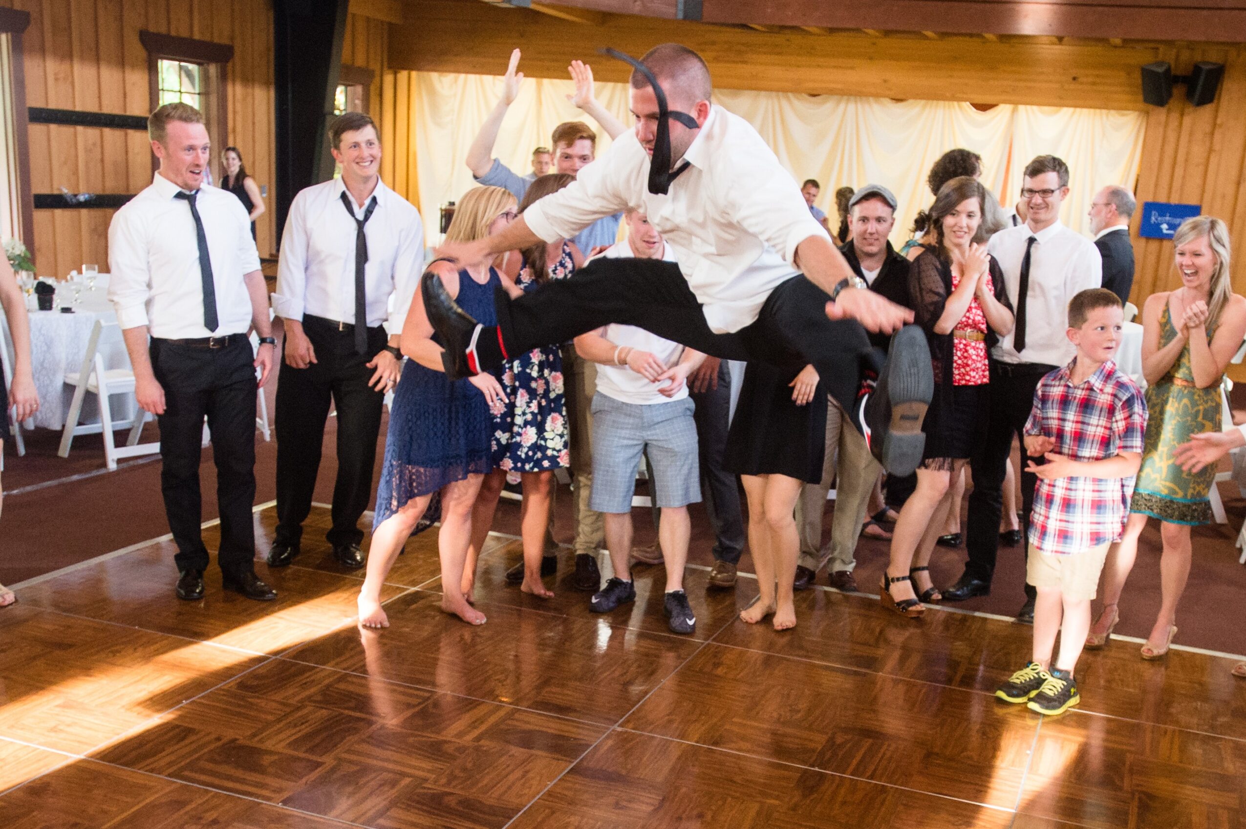 A man leaps across a dance floor as a group of people watch and clap.