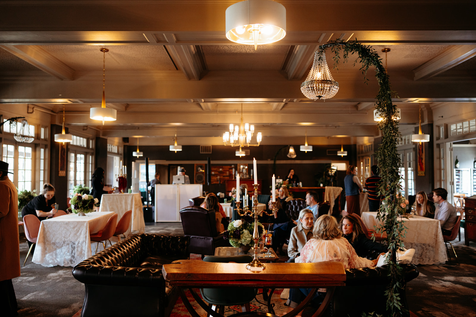 Restaurant dining room with tables, chairs, hanging lights, and several people seated together.