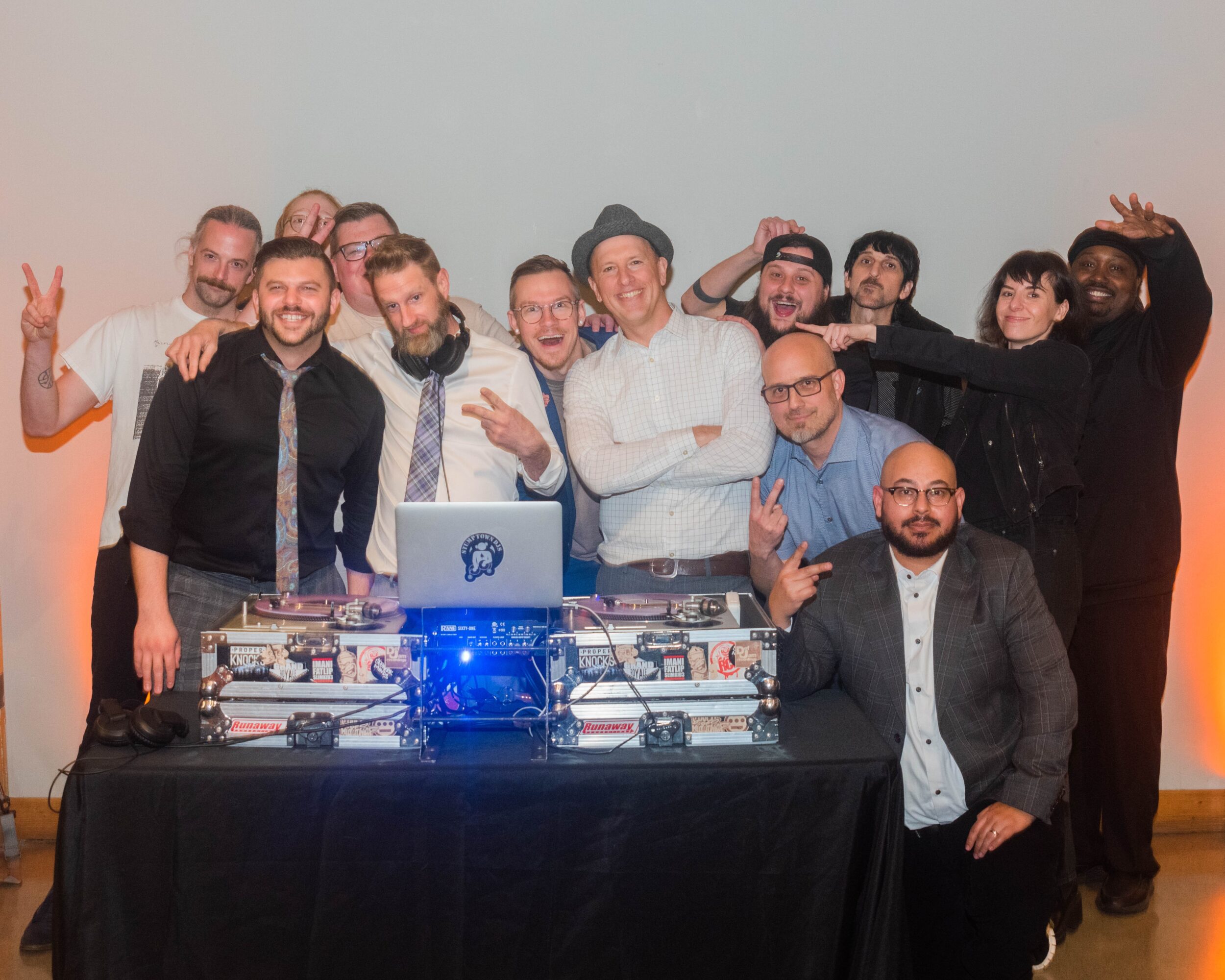 A group of people pose behind a table of audio equipment and a laptop.
