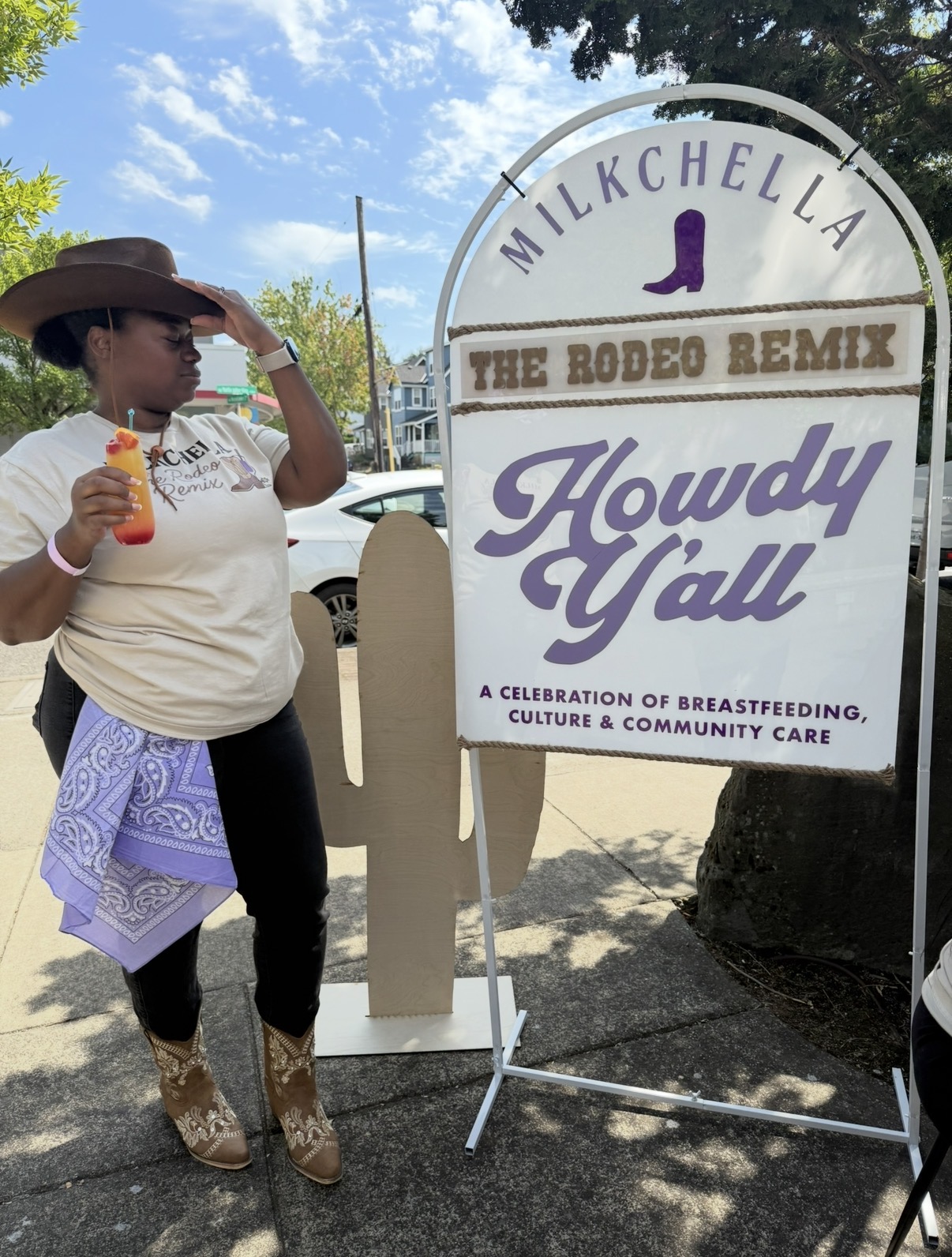 Person in a hat stands beside a sign reading “Milkchella,” “The Rodeo Remix,” and “Howdy Y’all.”