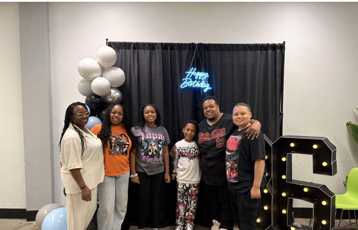 Six people pose in front of a black curtain with a blue neon sign and black-and-gold number decorations.
