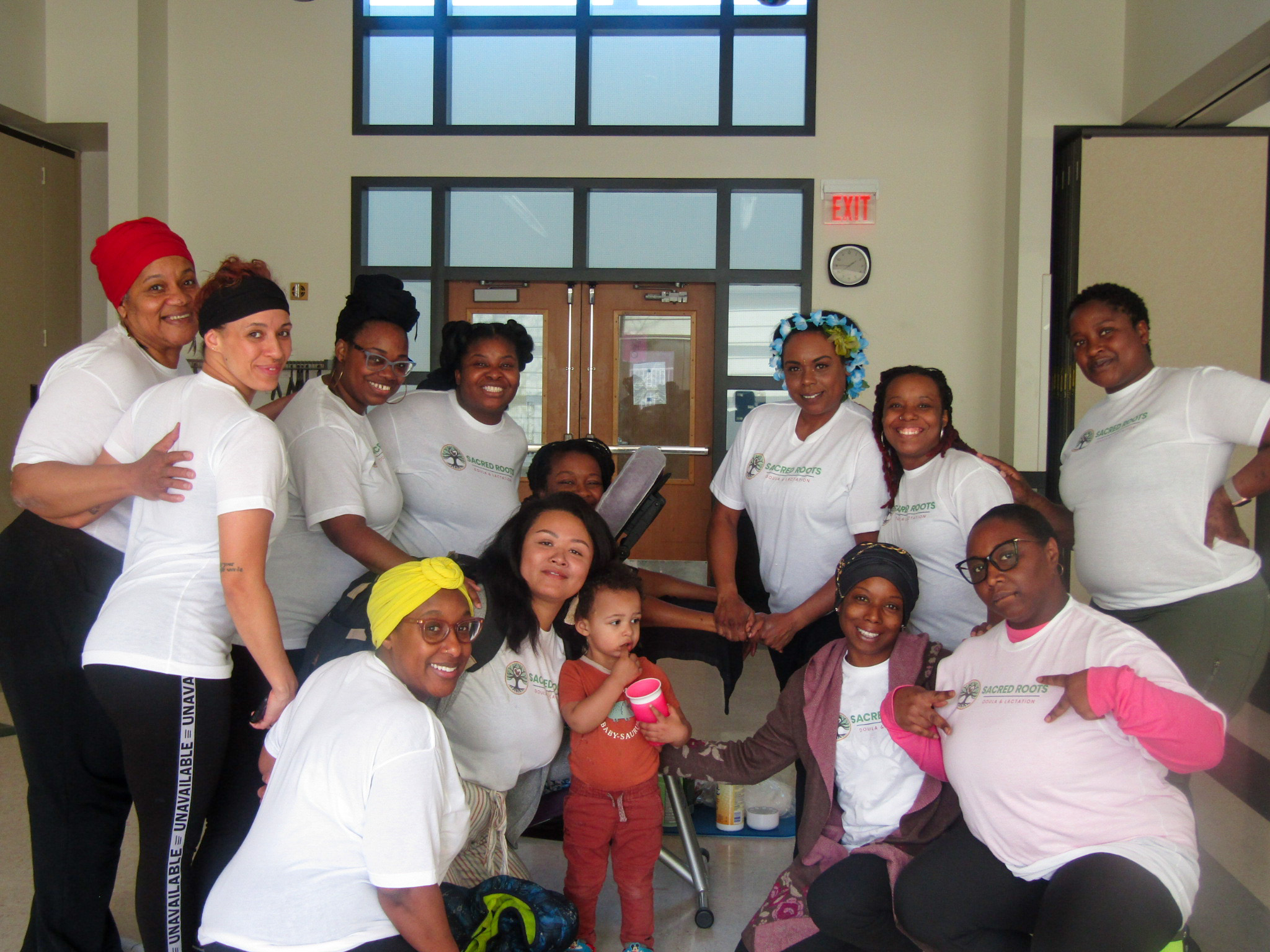 A group of people pose together in a hallway, with a small child standing near the center.