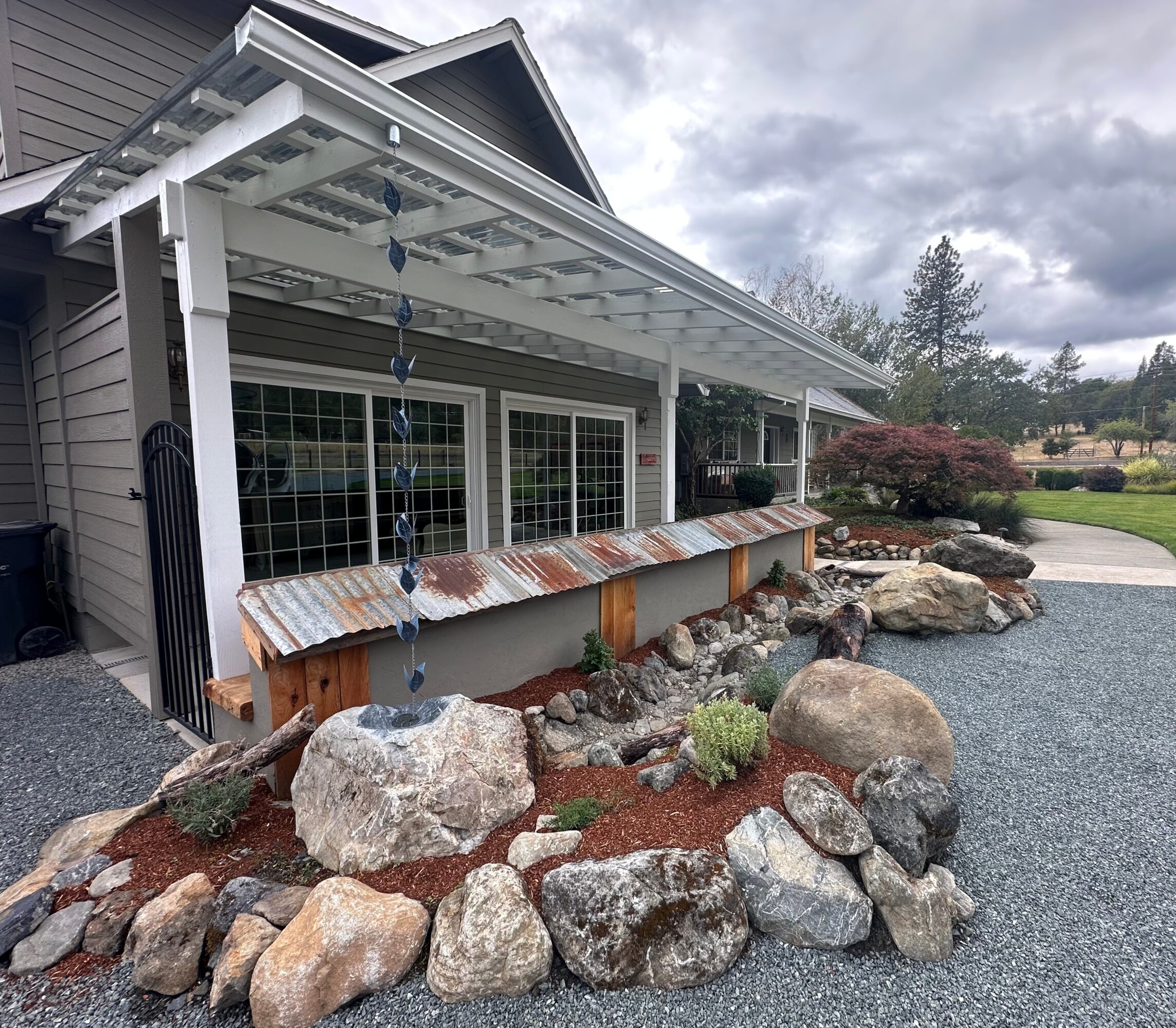House with a white covered patio, large windows, and a rock garden along the gravel driveway.