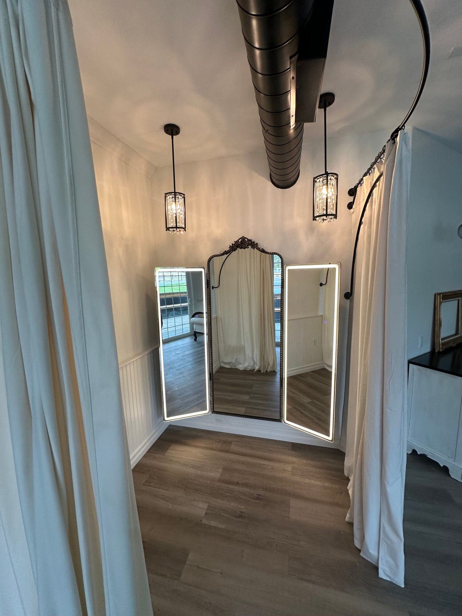 A room with two windows, a ceiling fan, string lights, and a wooden floor.