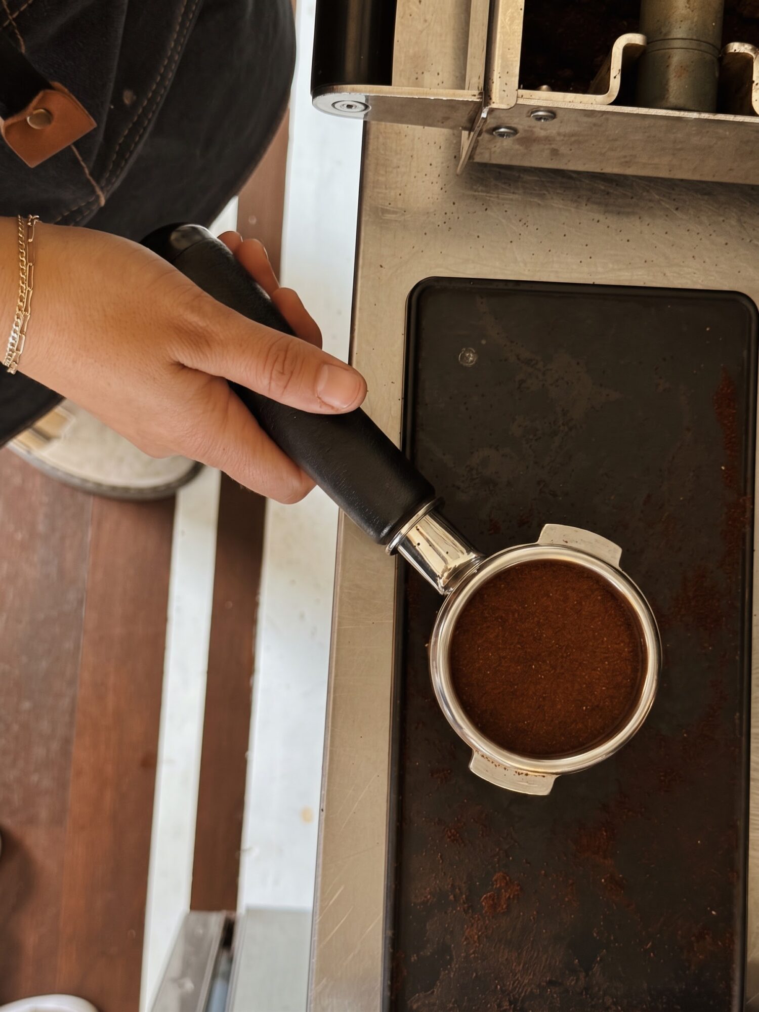 A person holds a portafilter over a coffee machine's dark drip tray.