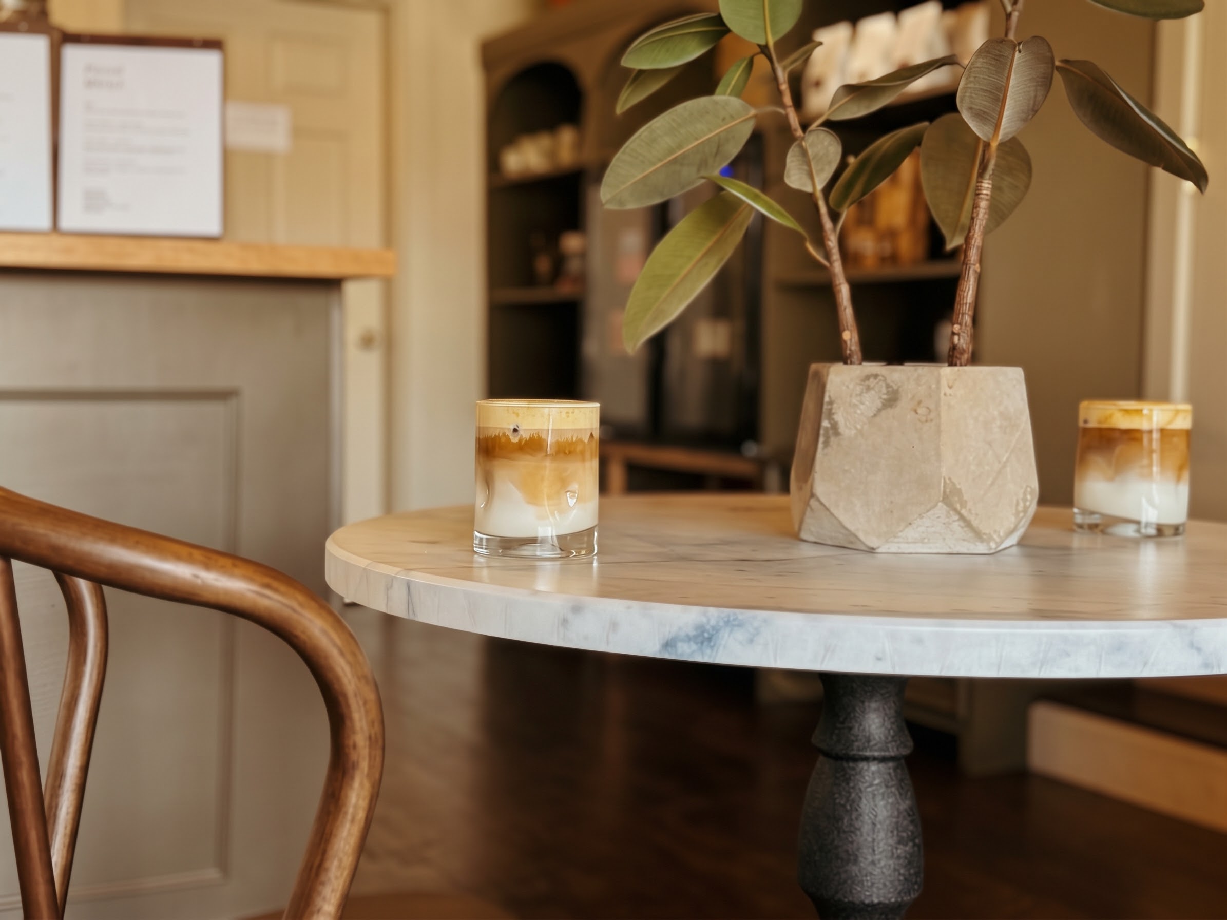 A potted plant and two glasses sit on a round table beside a curved wooden chair.