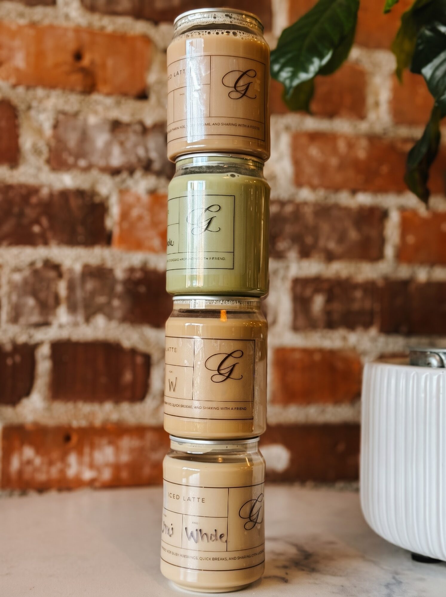 Four labeled jars stacked on a countertop in front of a brick wall, with a white ribbed planter beside them.