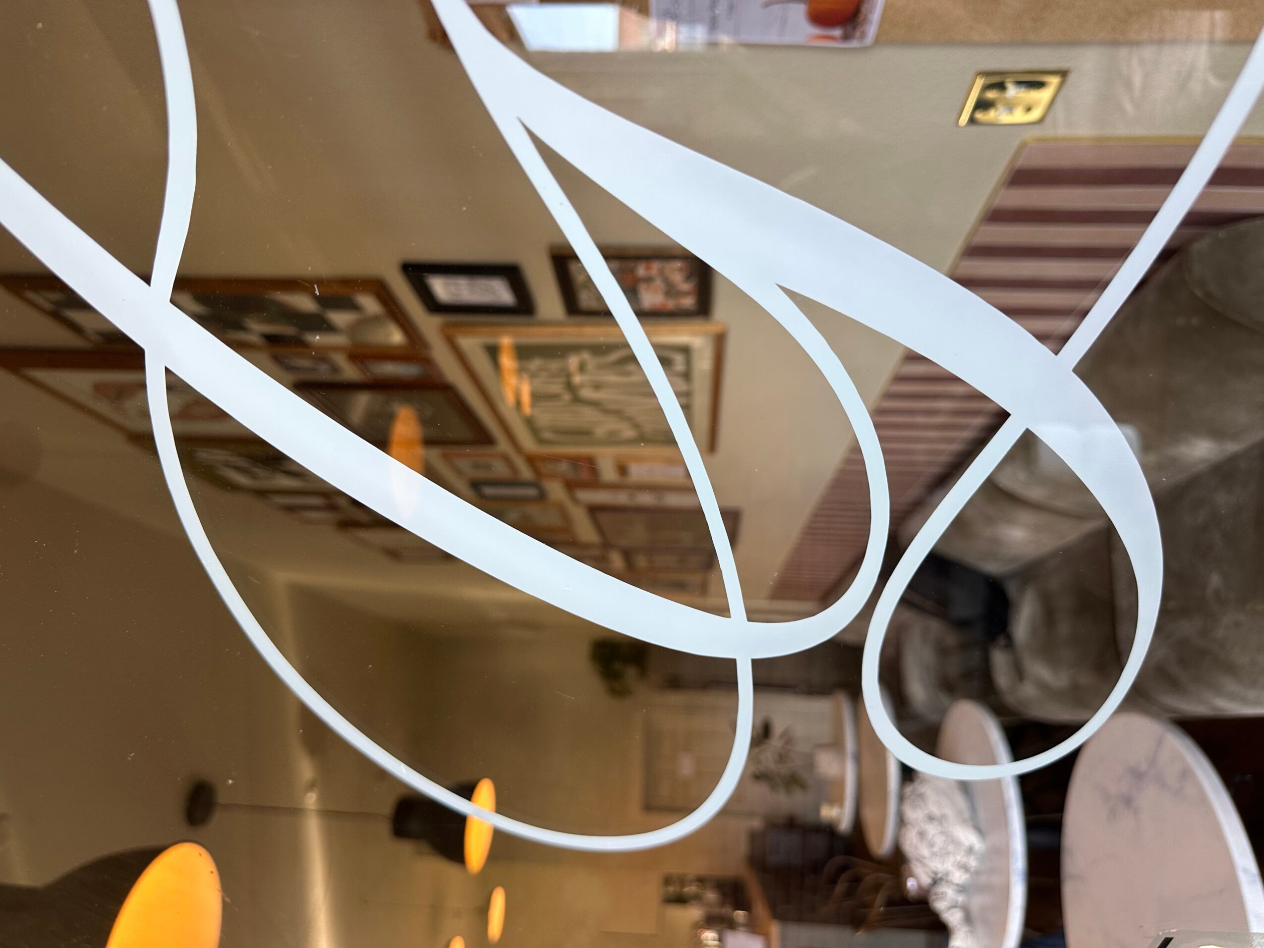 White curved lines across a glass surface, with framed pictures and a room reflected behind them.